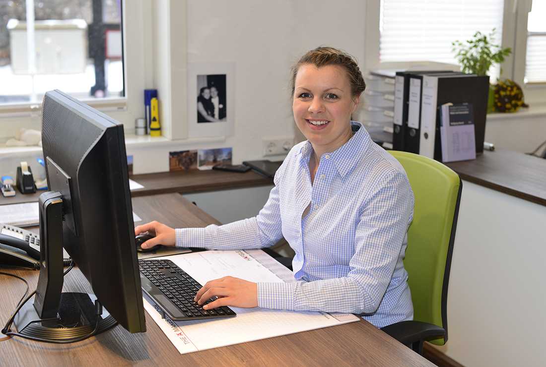 Lächelnde Christina Maier arbeitet an einem Schreibtisch im Büro